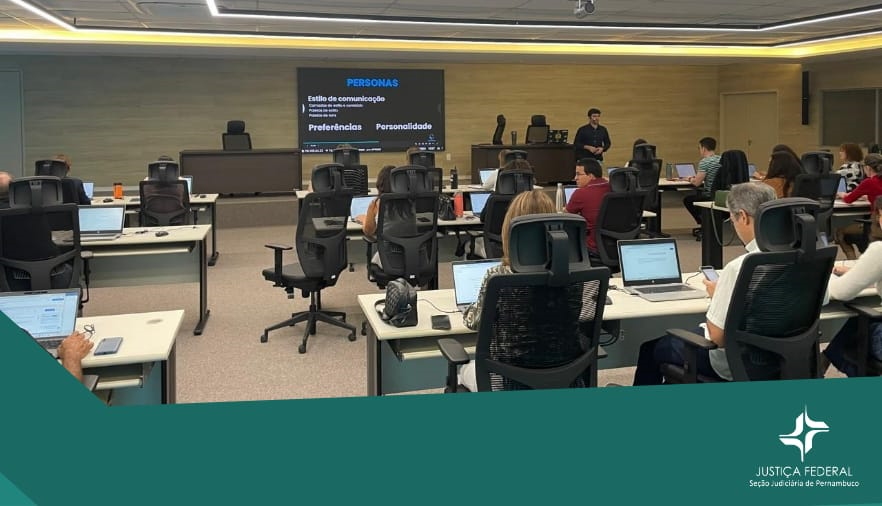 Imagem mostra pessoas em um auditório, com computadores